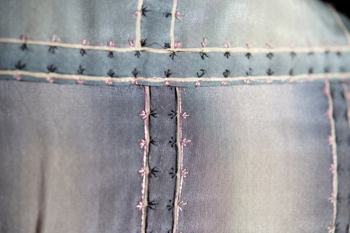 Av blågrått siden. Handbroderad med rosa och svart silke. Handtryckt sidenfoder med blom- och bladmotiv.