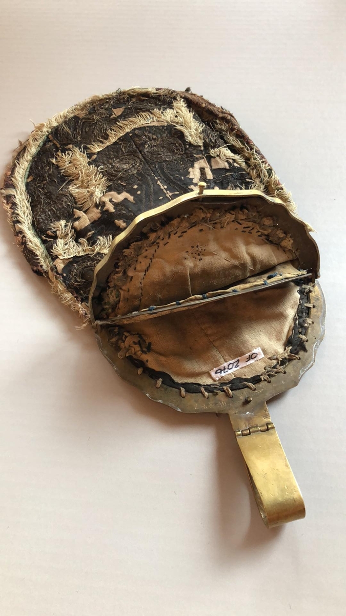 Løslomme/lauslomme i svart silke med metallbroderi og dekorbånd. Baksida er av svart ulldamask, og fôret er av ubleiket linlerret. Lommeposen er delt i to rom med delevegg av skinn.