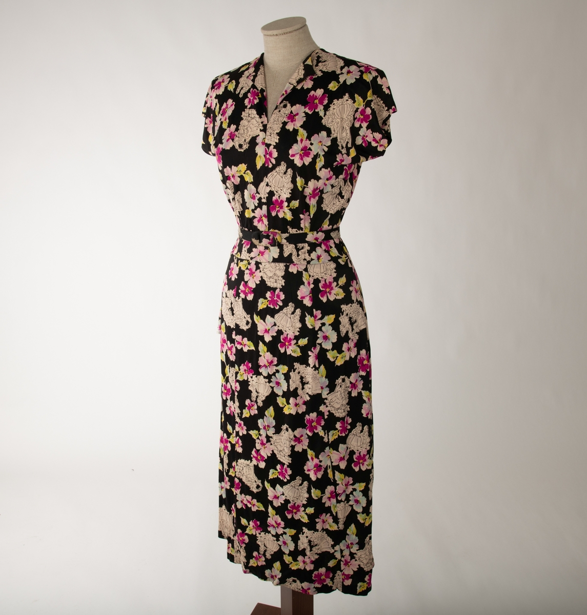 En svart kjole med et mangefarget motiv av blomster og en mann og en kvinne i ulike scener, begge kledd i 1700-talls overklasse-klær. Kjolen er ermeløs og krageløs. En glidelås under venstre arm går ned et lite stykke. Under denne er det et en splitt. Under halsen er det felt inn et svart gjennomsiktig stoff. Et hekte og en hempe i nakken skal lukke kjolen der, men hempe har røket

Det hører til et belte som er kledd i samme stoff.