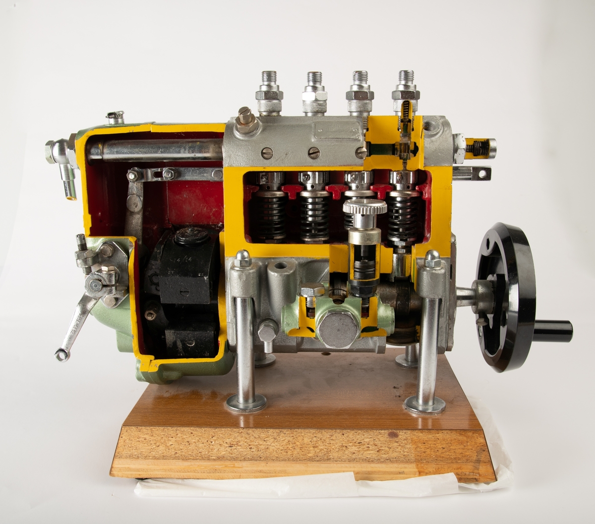En modell av en rekkemotor montert på en trebase. Modellen viser tverrsnittet av en motor. Ved å sveive på håndtaket går fire stempler opp og ned og viser hvordan en rekkemotor fungerer. Modellen er laget av grønnlakkert stål. Der metallet er "skåret" over" for å visse innholdet er det malt gult, innsiden er malt rød. Frontplaten på trebasen mangler, antagelig har det stått informajon om motortype her. Et klistremerke på baksiden angir produsent. En svart sveiv på siden er laget av plast.
