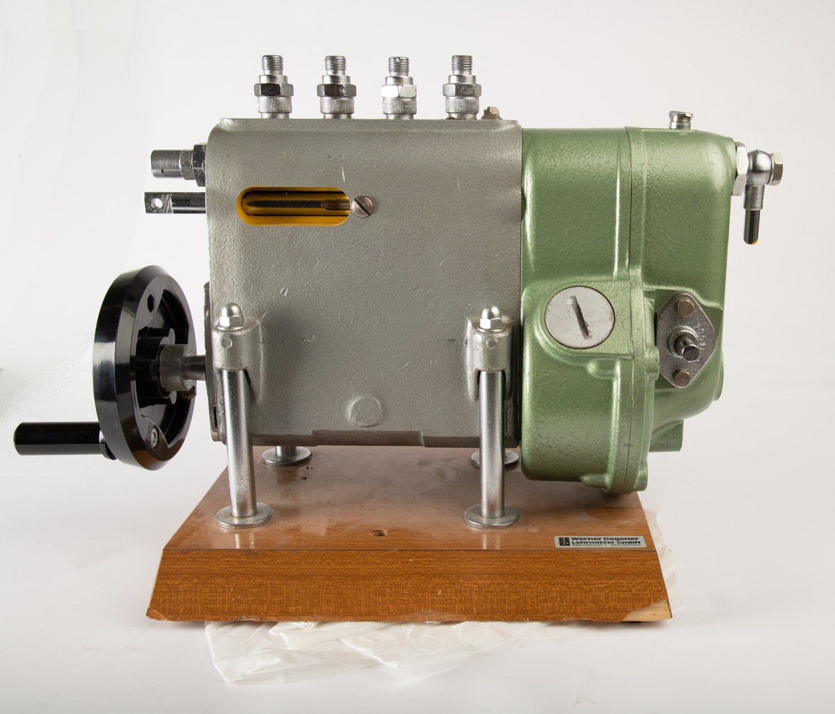 En modell av en rekkemotor montert på en trebase. Modellen viser tverrsnittet av en motor. Ved å sveive på håndtaket går fire stempler opp og ned og viser hvordan en rekkemotor fungerer. Modellen er laget av grønnlakkert stål. Der metallet er "skåret" over" for å visse innholdet er det malt gult, innsiden er malt rød. Frontplaten på trebasen mangler, antagelig har det stått informajon om motortype her. Et klistremerke på baksiden angir produsent. En svart sveiv på siden er laget av plast.