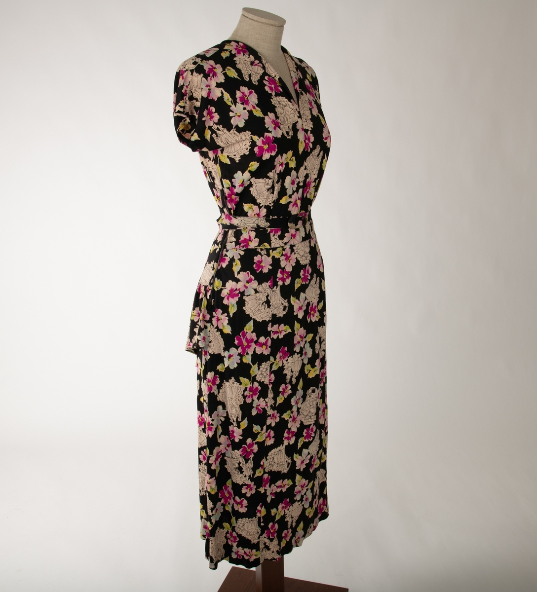 En svart kjole med et mangefarget motiv av blomster og en mann og en kvinne i ulike scener, begge kledd i 1700-talls overklasse-klær. Kjolen er ermeløs og krageløs. En glidelås under venstre arm går ned et lite stykke. Under denne er det et en splitt. Under halsen er det felt inn et svart gjennomsiktig stoff. Et hekte og en hempe i nakken skal lukke kjolen der, men hempe har røket

Det hører til et belte som er kledd i samme stoff.