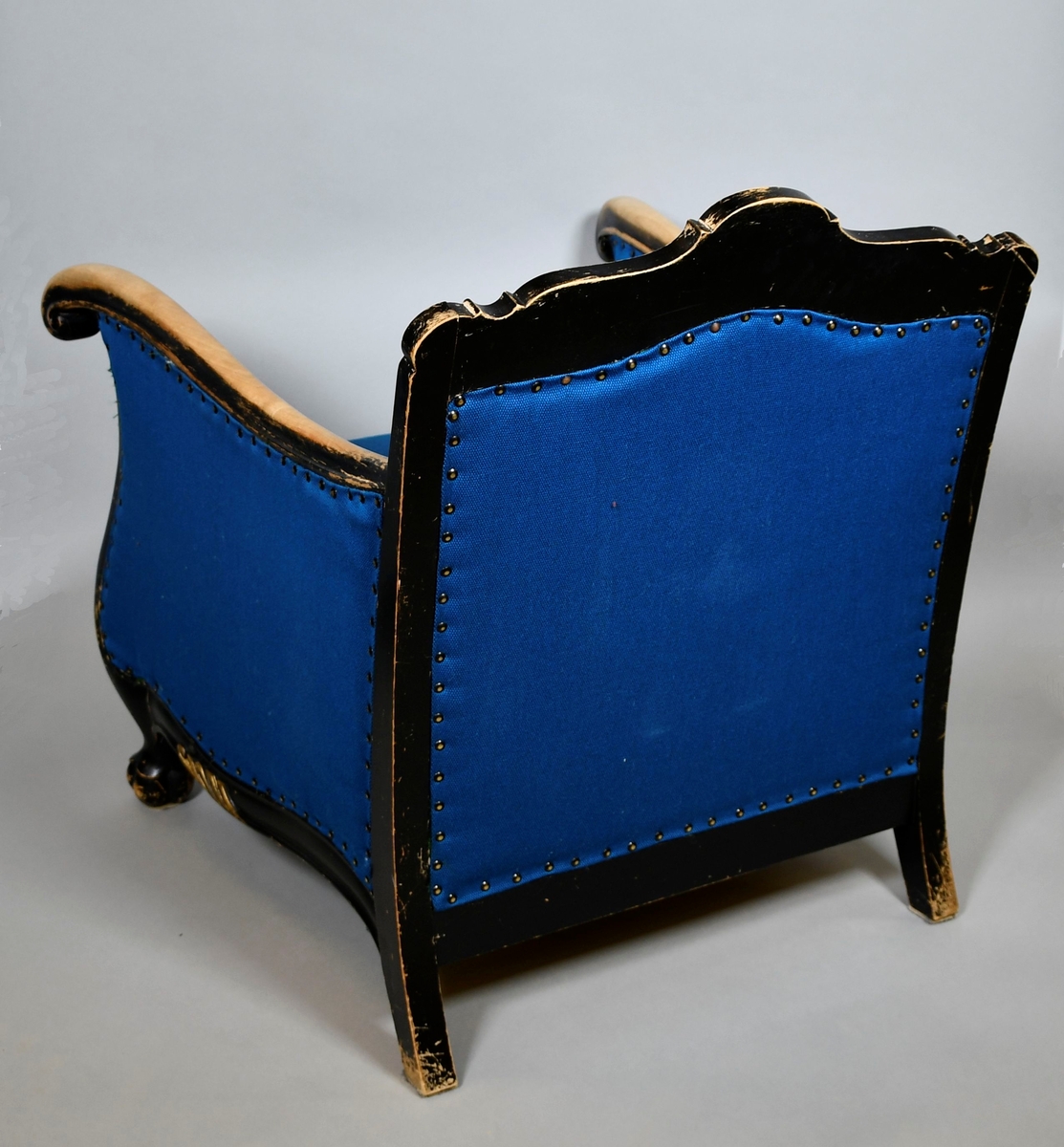 Barokkinspirert lenestol. Treverket har svart grunnfarge som er avslitt flere steder, spesielt på armlenene. Toppen av ryggen har symmetrisk skåret dekor av akantusranker, og et stående skjell i midten. Randen har bølgete form. Armlenene har kurvet form, og nederst på håndtakene er det volutter. Sprossen under setet har liggende skjell med to volutter på toppen. Treskåret dekor er gullfarget. Stolen har nytt, blått trekk.