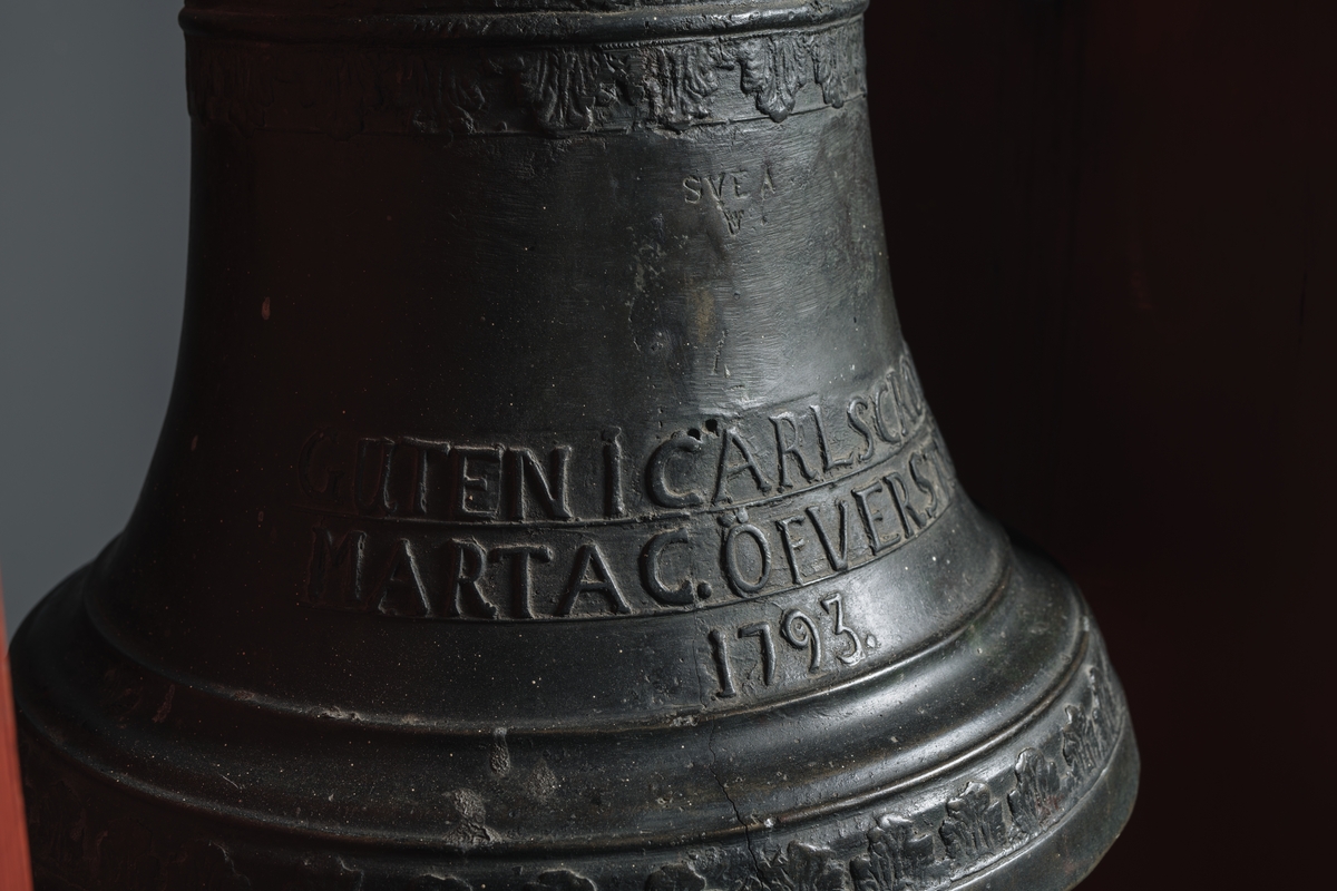 Skeppsklocka, av metall, gjuten år 1793, med följande inskription å ena sidan: "Gjuten i Carlskrona hos Marta C. Öfverström 1793". Å andra sidan ett namnchiffer "RGA" med kunglig krona över.
