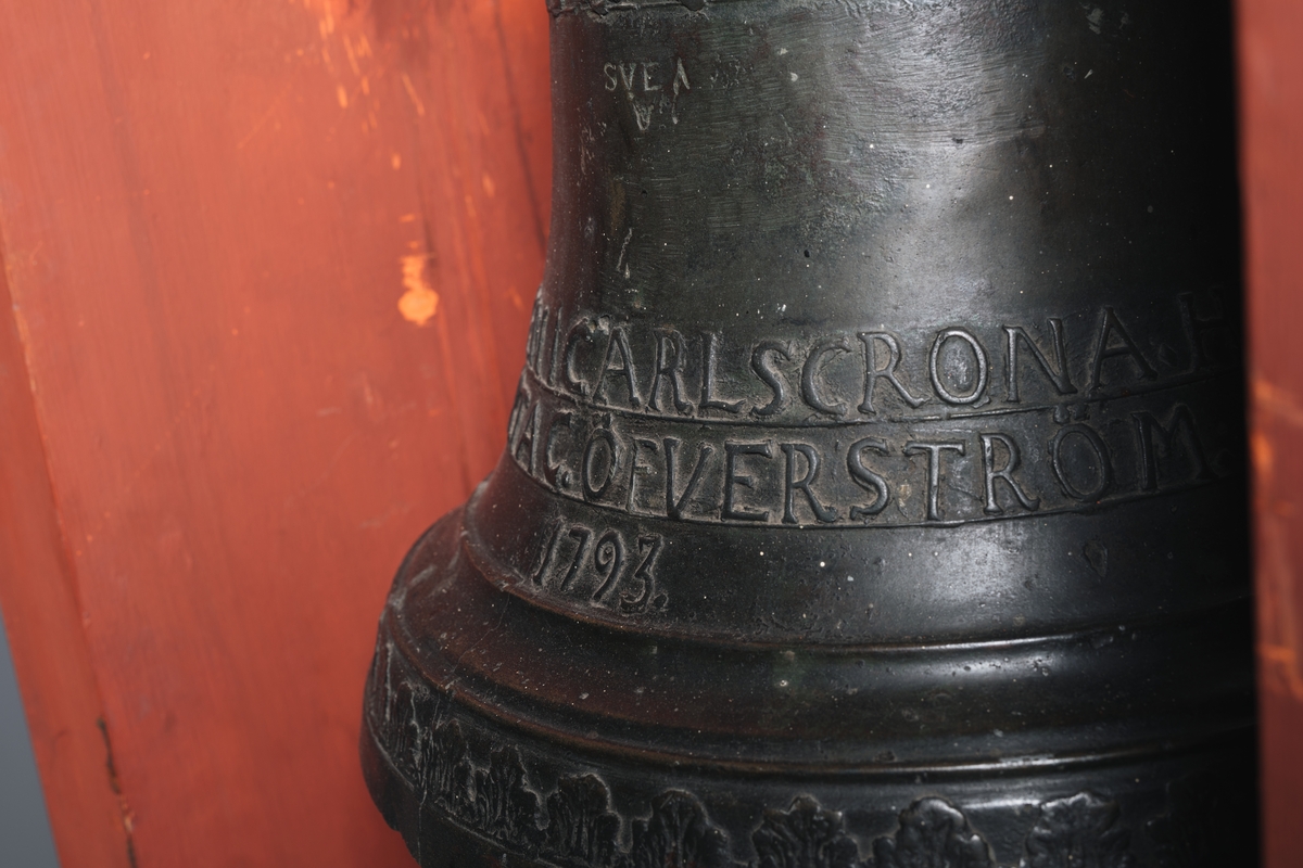 Skeppsklocka, av metall, gjuten år 1793, med följande inskription å ena sidan: "Gjuten i Carlskrona hos Marta C. Öfverström 1793". Å andra sidan ett namnchiffer "RGA" med kunglig krona över.