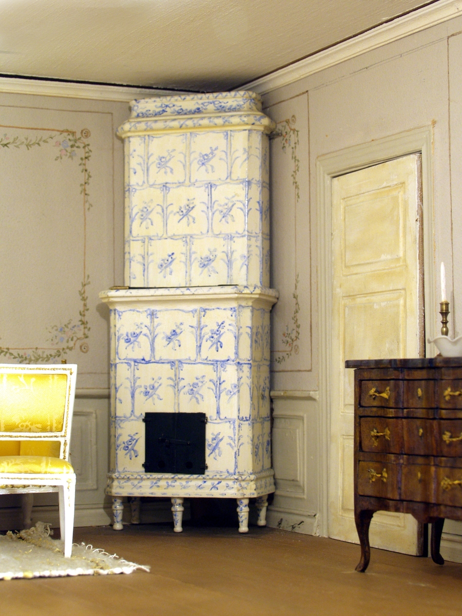 Vägg med panelbeklädd nederdel, överdel med handmålade fält med ramar och blomrankor. Två fönster med spröjsade rutor, kornisch med gardin, två längder och en kappa. Vit kakelugn med blått rutmönster, svarta luckor. Bredvid kakelugnen en eldgaffel. Dörr med tre speglar. Plankgolv, vitmålat tak. Sittmöbel bestående av soffa (jfr 34 076), ovalt bord på fyra ben med urna på benställning, fem stolar två vid soffa och bord tre vid vägg. Möbeln vitmålad med guldfärgade dekorationer, klädsel i gult blankt tyg. På bordet spetsduk och blommor i glasvas samt bricka med karaff och sex glas. Beige matta med brun rand vid varje ände. Byrå med tre lådor, vågformad front, brunbetsad med guldfärgade beslag. På byrån två ljsstakar med ljus och en vit porslinsskål. Två speglar, en mindre, placerad snett ovanför byrån, guldfärgad ram krönt med rosett, en större, placerad mellan fönstren, delat glas, guldfärgad ram krönt med urna. Under spegeln ett fönsterbord (jfr 34 071), guldfärgad underdel, skiva med marmorimitation. På bordet ljusstake med ljus. Under varje fönster ett sybord (jfr 34 073). Rektangulär bordsskiva med avskurna hörn, underrede i form av lyra med strängar av metall samt figursågad fot. På varje bord en rund spetsduk. På ena bordet blommor i vas. I ena fönstret 3 krukväxter, i det andra två. Gipsbyst på kolonnformad sockel.
Ovan nämnda byst hämtades i Italien av Berith Bergströms brorson Ingmar Bergström.
Belysning i form av en glödlampa vid framkanten insatt vid senare datum då skåpet placerats i ett montage med skåp nummer 34 049-34 054.