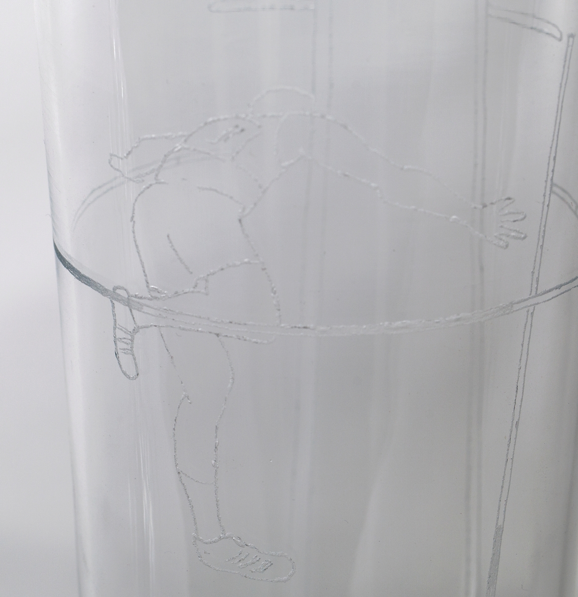 Pokal med lokk i klart glass, dekorert med gravering i form av stiliserte atleter. 

1) Høyreist sylinderformet korpus som hviler på en kuleformet stett, samt noe hevet sirkulær fotplate. På øvre del av korpus er det gravert en mannlig atlet som utfører friidrett, trolig stavsprang.

2) Tilnærmet sylinderformet lokk med høyreist kuleformet lokknapp, flankert av to mykt buede glasstaver med påklipp.