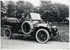 En man i kavaj och keps poserar i sin bil, parkerad på en grusväg vid Kronobergs kungsgård, ca 1920.