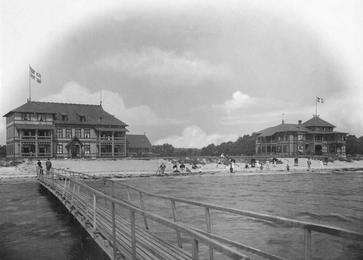 Ystad saltsjöbad sett utifrån en brygga. Badgäster på stranden. Bilden deltog i 1899 års pristävling anordnad av Svenska Turistföreningen.
