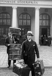 Två män framför Stockholms central, båda bär på bagage, resv