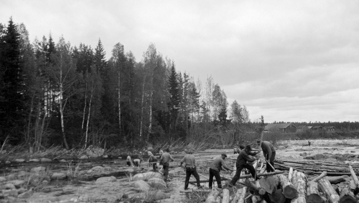 Fløtingsarbeid i Grundsetfossen i Glomma, et par kilometer nord for kommunesenteret i Elverum i Hedmark.  Fotografiet er tatt i slutten av mai 1928.  Vi ser ei gruppe fløtere som, med fløterhaker som arbeidsredskap, trekker stokker som har blitt liggende på ei steinør i den vestre delen av elvefaret.  Problemet oppsto antakelig da vannstanden i elva sank.