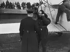 En militär och en flygförare står vid flygplan S 6 Fokker på ett flygfält.