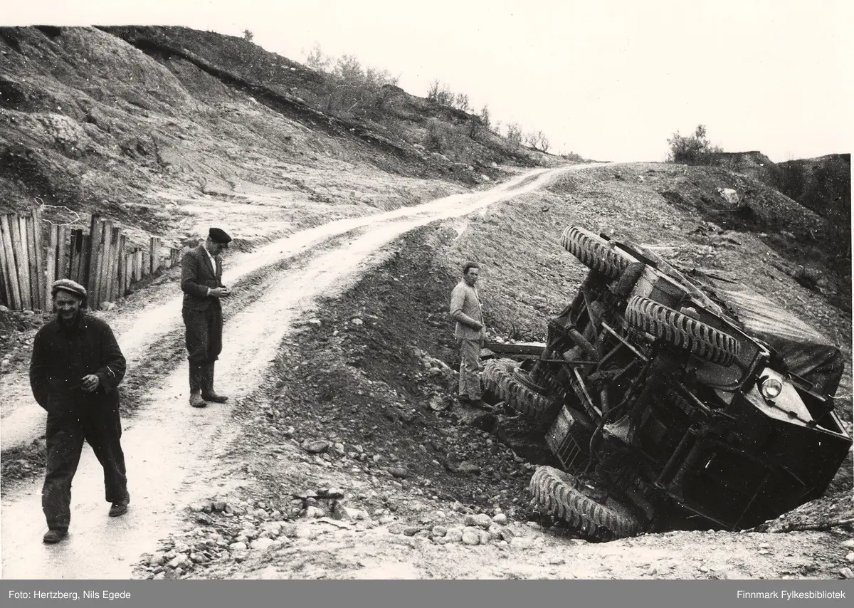 R.v. 50. 5 km. vest for Kunes, 1948. Leirbakken. Det var gått et leirras tidligere og veglinja ble flyttet lengere ut fra bakken. Masseflyttingen ble foretatt med Bulldoser. En militærbil har kjørt ut av veien. Vegskjæringen er stemplet av med planker. Veglinjen forbi rasstedet. Skråningen gled ut og bilen seg ned i skråningen. Ingen ble skadet. Fra venstre: Johannes Foslund, Kåre Foslund. Personen ved bilen er ukjent. Lastebilen er en Fordson WOT.