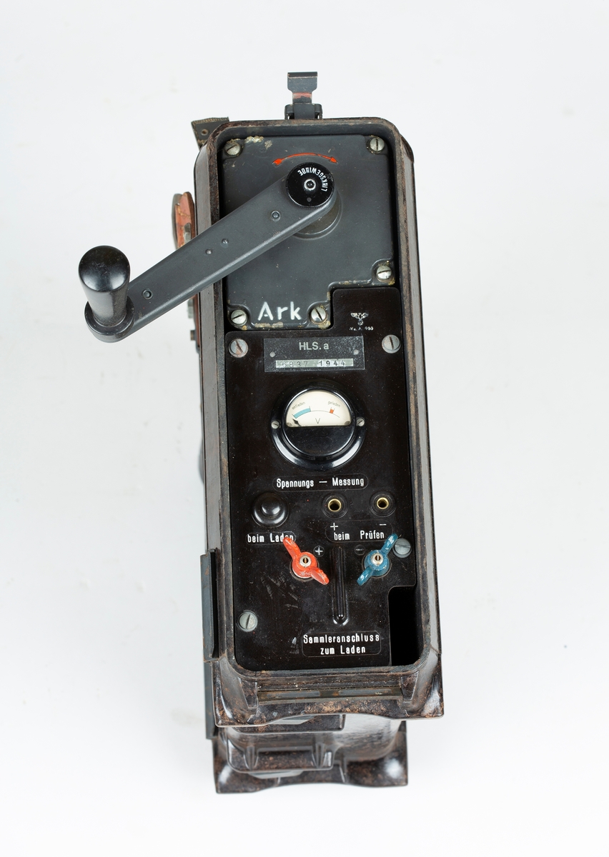Transportabel generator med sveiv, to kabler. Tyskprodusert, antagelig fra 2. verdenskrig. Til radio og telefonsamband. Tysk bruksanvisning på sidelokk.