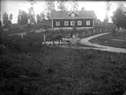 Pojke med häst och vagn vid ett trevägskors. På vagnen mjölkflaskor. I bakgrunden ett bostadshus.