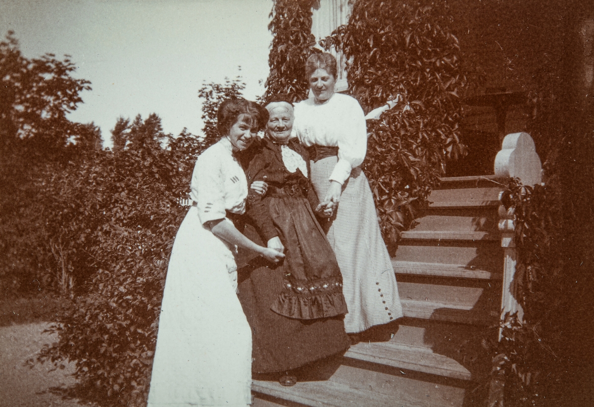 Gruppe 3 damer på trappen i hagen utenfor direktørboligen "Maihaugen" på Aadals Brug omkring 1910. Til venstre, Astrid Granzow (f 1885 i København), hun var Axel Sydbergs forlovede. I midten, Astrids mor,  Hulda Granzow (f 1842 i Lund, Sverige), på besøk fra Danmark. Til høyre Axels mor, Julie Anna Clara Syberg. Direktørboligen ble oppført i 1897, og brant i 1914.