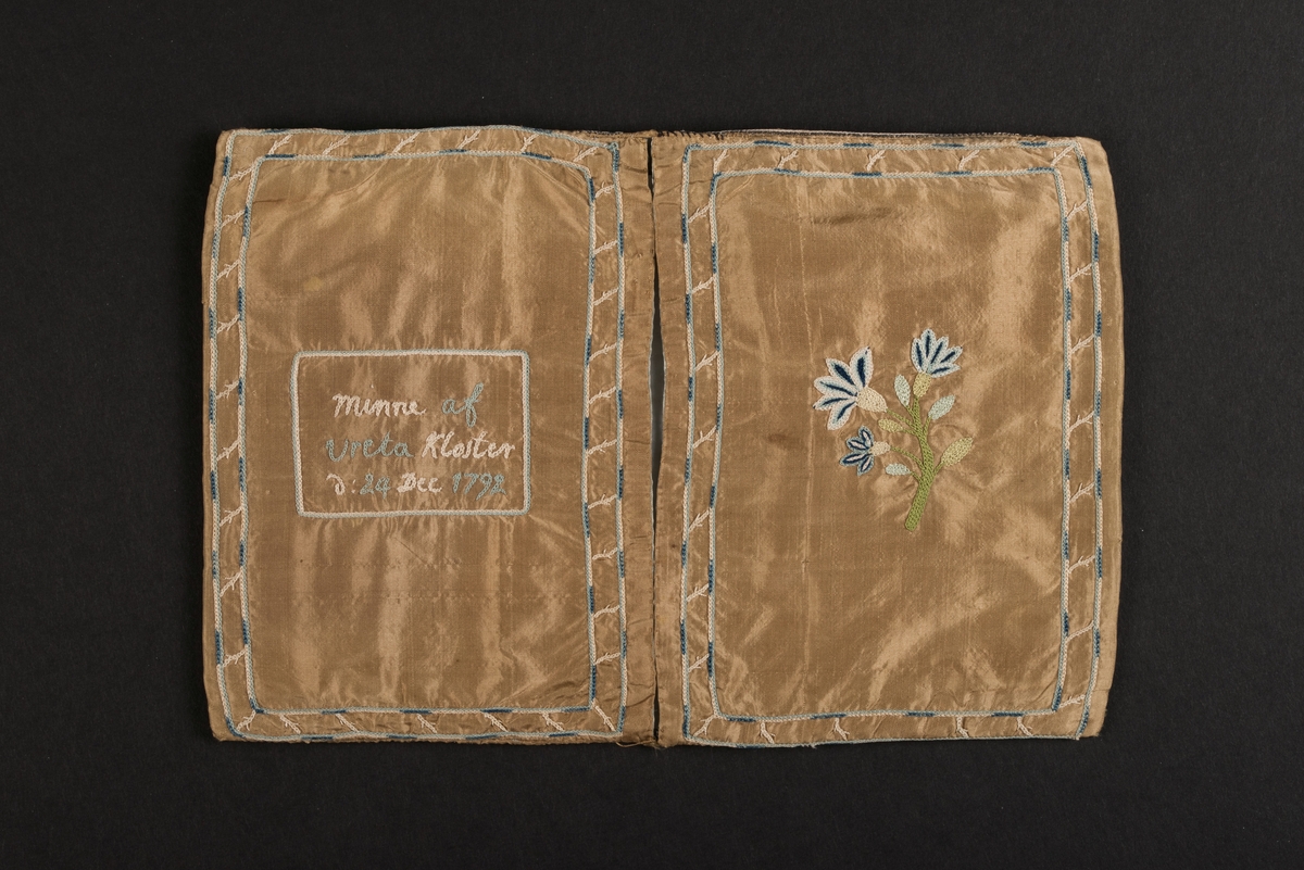 Plånbok, även kallad sedelbok, med två fack, av siden. 
Dekorerad med broderier av silkestråd i kedjesöm. Det bruna sidentyget har broderade kantbåder. På utsidorna blomsterbroderier och på insidan blomsterbroderi på ett av de två facken. På det andra facket finns en broderad text inom ram: Minne af Vreta Kloster d: 24 Dec 1792.