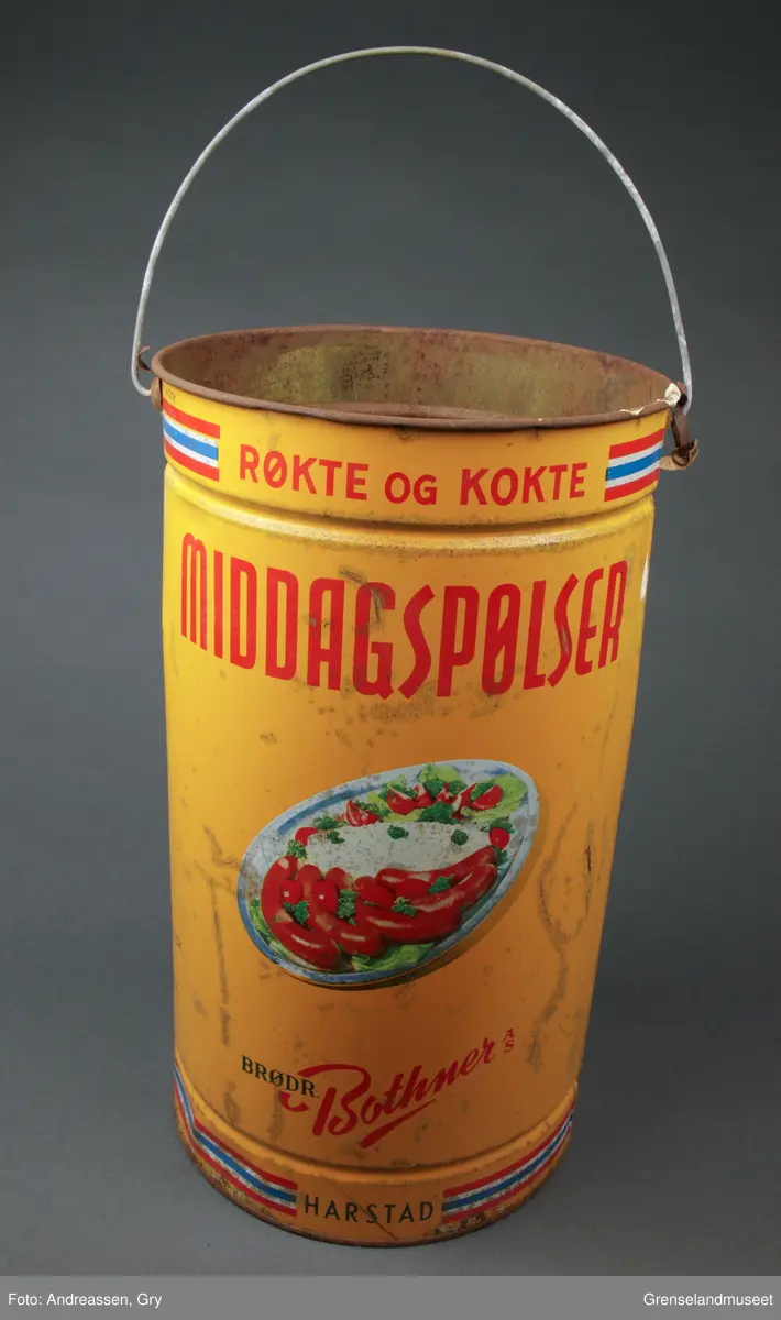 Pølsespann fra Brødrene Bothner AS, 10 kg. Bilde av fat med pølser og potetstappe og tomater. Randdekor oppe og nede med fargene fra det norske flagget. Det er begynt å ruste hull i bunnen av spannet.
Oppi spannet ligger det flere forskjellige gjenstander:
- 1 Dekorert skaft i sølv, til bestikk. Merket med 830 S
- 1 knivblad, rustent
- 2 Volter, 6 cm lange
- 1 større skaft i lakkert tre med en metallring rundt hull for feste. Skaftet er 25,5 cm langt.
- 10 halvskiver i et hardt tremateriale. To av dem er delvis ødelagt, den ene er i to deler. Diameter nå de sette sammen er ca 20-22 cm. Størrelsen varierer litt.