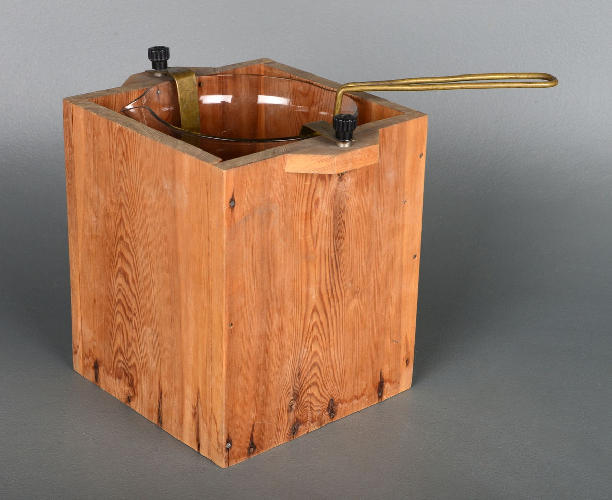 Instrument for å varme væske. En treeske med små håndtak på siden og glassbeholder inni. I esken er det festet åtte korkbiter for å holde glassbeholderen stabil. Det er to strøminnganger på håndtakene og metall som leder strømmen ned til varmetråder i bunnen. Inne i glassbeholderen er det et stativ man kan sette en kolbe eller lignende på og senke ned.