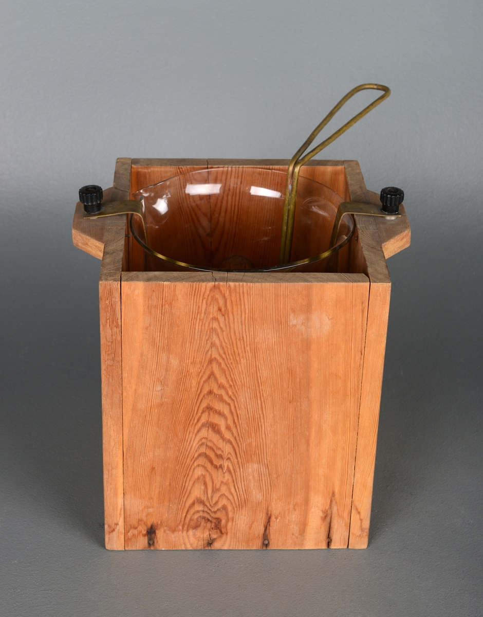 Instrument for å varme væske. En treeske med små håndtak på siden og glassbeholder inni. I esken er det festet åtte korkbiter for å holde glassbeholderen stabil. Det er to strøminnganger på håndtakene og metall som leder strømmen ned til varmetråder i bunnen. Inne i glassbeholderen er det et stativ man kan sette en kolbe eller lignende på og senke ned.