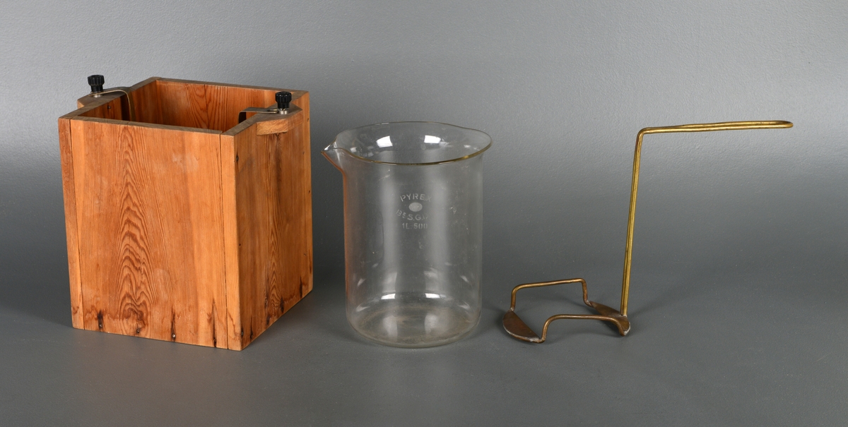 Instrument for å varme væske. En treeske med små håndtak på siden og glassbeholder inni. I esken er det festet åtte korkbiter for å holde glassbeholderen stabil. Det er to strøminnganger på håndtakene og metall som leder strømmen ned til varmetråder i bunnen. Inne i glassbeholderen er det et stativ man kan sette en kolbe eller lignende på og senke ned.