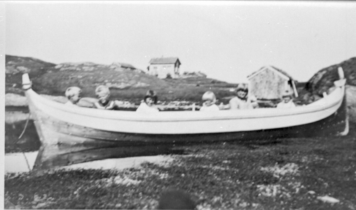 Seks barn sittende i nordlandsbåt i fjæra i Vika på Stangnes.