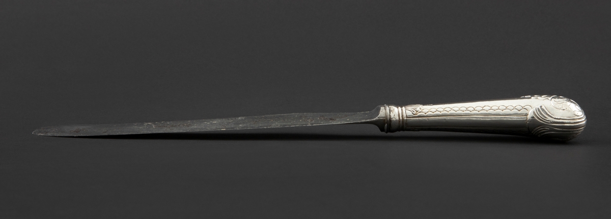 Kniv med sølvbelagt skaft og knivblad av stål. Knivbladet er flatt, buet med rund avslutning. Skaftet er rundt og dekorert med palmett- og bølgeornamentikk. Enden av skaftet er formet som et skjell med planteornamentikk.
