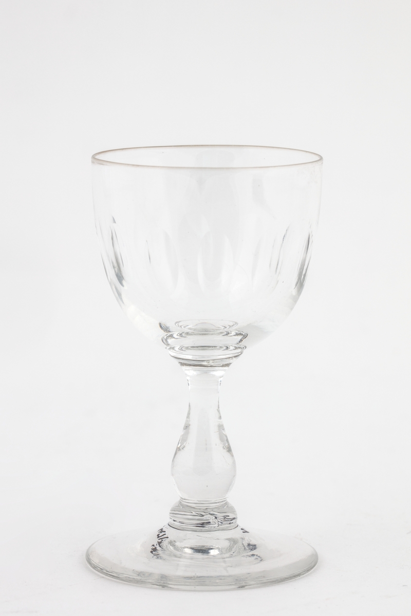 Vinglass (rødvinsglass) med rett klokke, pæreformet stett og flat fot. Enkel olivensliping rundt klokken, ellers udekorert. Klar farge. Glasset er i god stand.