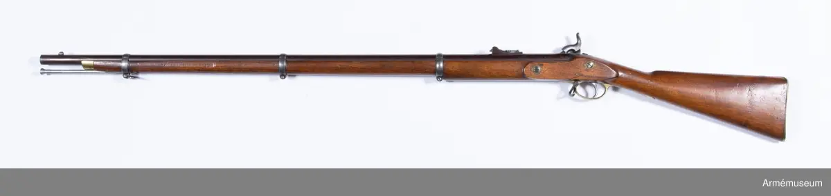 Grupp E II.
Gevär med slaglås.
Antal räfflor: 3. Räffelstigning: ett halvt varv på piplängden. Kulvikt: 34 g. Krutladdningens vikt: 4 g. Pipan är brungjord och rund, men har baktill på översidan en 3,5 cm lång avplattning. Snäckan är rätt liten. En fyrkantig kombinerad bajonett- och kornklack sitter 3,3 cm bakom mynningen och på översidan av denna klack sitter det orörliga kornet. Ramtrappsiktets fot sitter 8,9 cm framför pipans bakre ände. Siktet har gradering för avstånd mellan 100 och 900 yards= resp 90 och 810 m. På pipans översida står PRITCHETT 7 POULTRY LONDON och på vänstra sidan är två Londonstämlar inslagna.

På det gråhärdade, framåtliggande kedjelåset är hanen och låsblecket längs kanterna prydda med ett par ingraverade ränder. stocken är av valnöt. Framstocken har en avsats för vart och ett av de tre banden. Piprännan är utvidgad alldeles bakom näsblecket. Bakplåten och varbygeln är av mässing. Den förstnämnde har en ganska lång, smal flik, som går in över kolvryggen och som längst fram är fäst med en skruv, under det att två skruvar sitter i bakplåten. Geväret har egentligen ej sidbleck, utan kring vart och ett av de bägge hålen för låsskruvarna finns en smal, ringliknande mässingsskoning, från vilken en kort arm går framåt och en annan bakåt. De tre banden är av gråhärdat järn och ha på undersidan öron, som förenas genom en skruv. Det främsta bandet ligger 8 cm bakom stockens framände och skruven på detta band fasthåller den främre rembygeln. Näsblecket är av mässing, och fasthålles av en underifrån kommande skruv. Den bakre rembygeln är fäst i varbygelns främre del.

Laddstocken är av stål och har skålformigt huvud. Omkring 12 cm från framänden har laddstocken en ungefär 2,5 cm lång förtjockning, som passar i laddstocksrännans ovan omtalade utvidgning. I smaländen är laddstocken gängad på en längd av 0,8 cm. Litet bakom huvudet finns fyra nästan utslipade bokstäver (R & K?).

Om den till detta gevär använda ammunitionen, se AM 6117-6120. Uppgiften om reffelstigningen har hämtats ur Jochnick, Handgevärslära, Stockholm 1863 paragraf 60. Geväret kallas vanligen Enfield- pritchetgeväret, då det konstruerades av gevärsfabrikanten Pritchett och antogs av den i Enfield församlade gevärskommiten. Av allt att döma har alltså den ovan beskrivna gevär tillverkats av konstruktören.