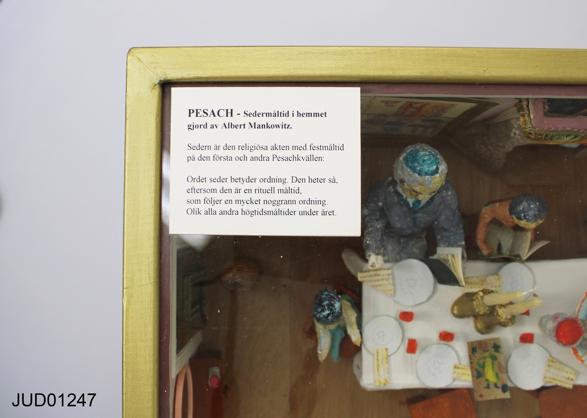 Pesachscen med dockor i glasmonter, betitlad "Sedermåltid i hemmet".