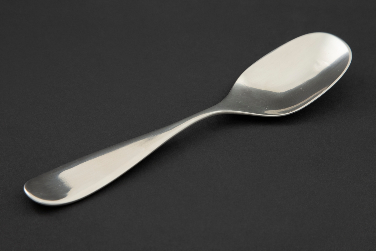 Serveringsskje i mattpolert rustfritt stål. Ovalt skjeblad med smal legg og dråpeformet skaft med oppbøyd, avrundet ende.