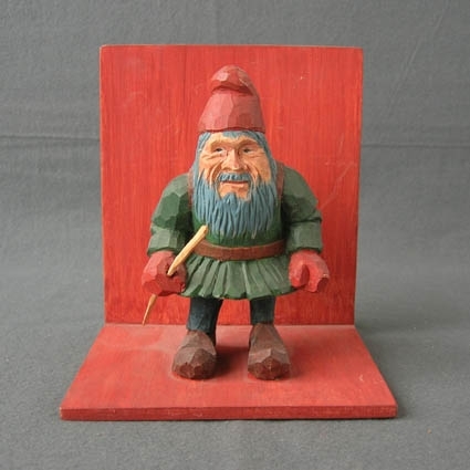Tomte på en hylla. Figuren är täljd ur ett trästycke. Hyllan är tillverkad av kryssfaner och målad brunröd.