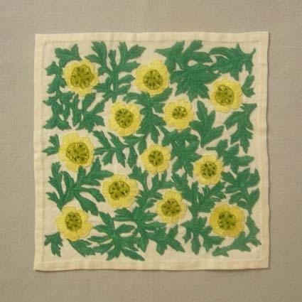 Broderad tablett med ljusgula blommor och gröna blad broderade i langettsöm med knutsöm i blommornas mitt. Tabletten är handfållad.Motivet på tabletten liknar ACVLH 1342 och ACVLH 1411