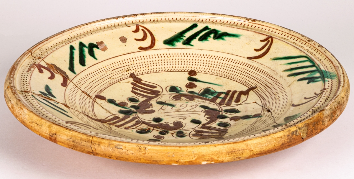 Lerfat, invändigt glaserat i gult, dekor i brunt och grönt. 1799, spräckt.