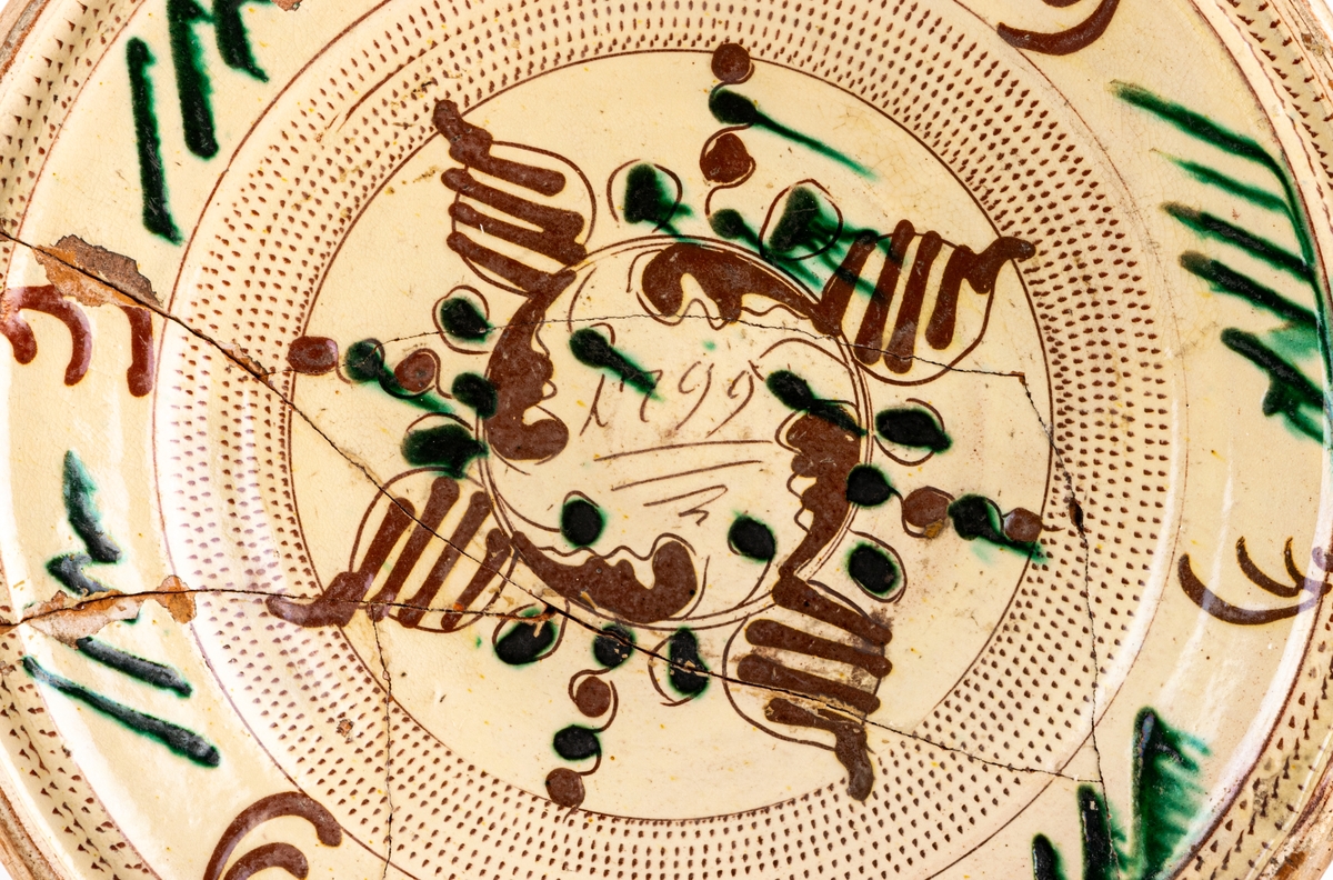 Lerfat, invändigt glaserat i gult, dekor i brunt och grönt. 1799, spräckt.