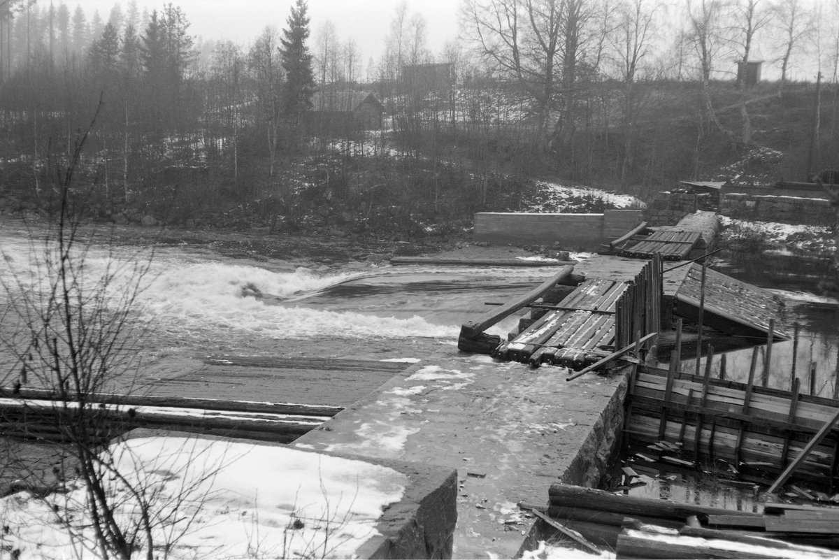 Fra Kjellåsdammen i Flisavassdraget i Åsnes i Solør. Her er dammen fotografert fra østre mot vestre elvebredd en dag i 1964. Dammen er murt av kvadret naturstein som er forsterket med betong. Den har to løp. Det ene av disse var stengt med nåler, vertikaltstilte planker som var reist mot en terksel på elvebotnen og mot morstrøms side av dambrua.  Kjellåsdammen er en terskeldam som skal stuve opp vannet på morstrøms side og dermed redusere faren for at løstømmer som kommer flytende fra ovenforliggende skoger skal strande på sandbanker eller grusører i elveløpet.