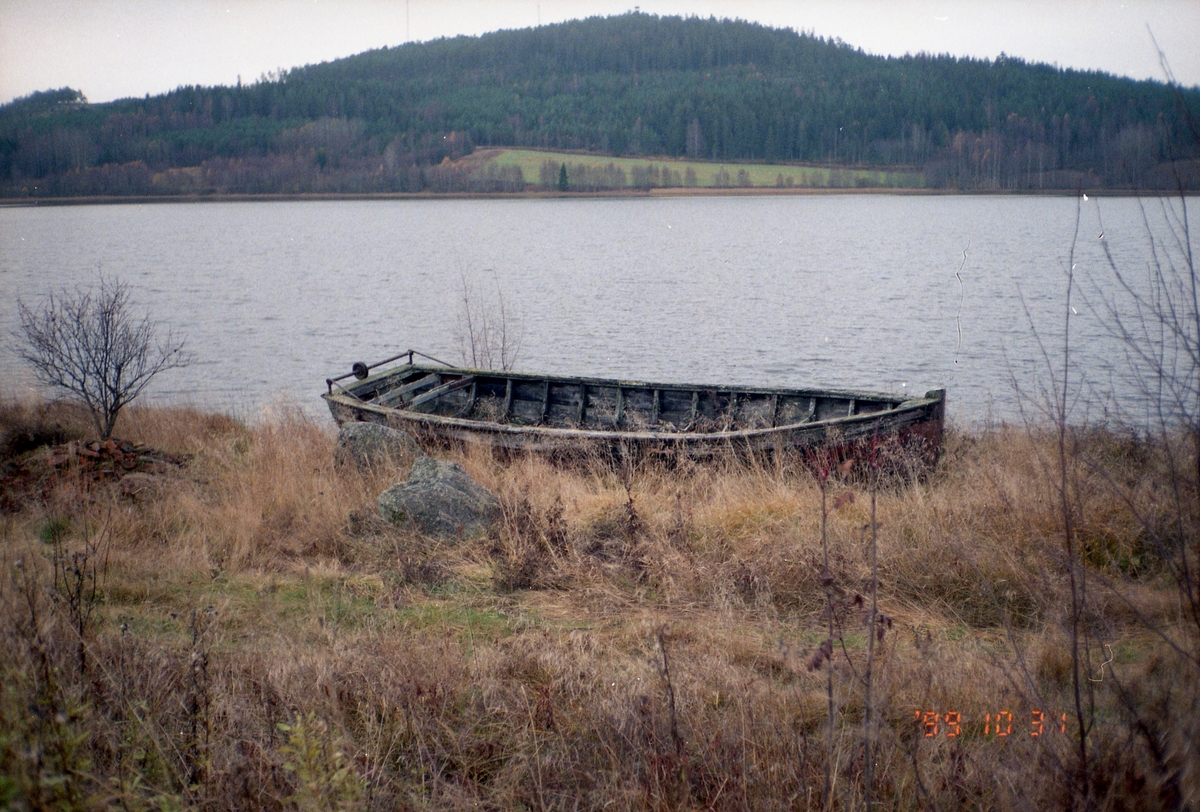 En båt ligger uppdragen på land vid en sjö med berg i bakgrunden, 31 oktober 1999.