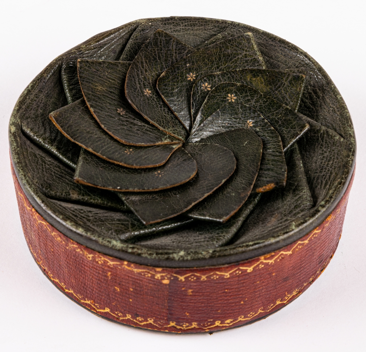 Tobaksask, låg, rund pappask, med botten av papp och lock av skinn skuret med snibbar och vridet koncentriskt så att snibbarna bilda en tiouddig figur. Sidorna röda, ovansidan skinnet grönt. Smala guldbårder på askens sidor och texten "Joh. Olof Norin", samt små guldstjärnor på ovansidan skinnet. Skinnet är saffian.