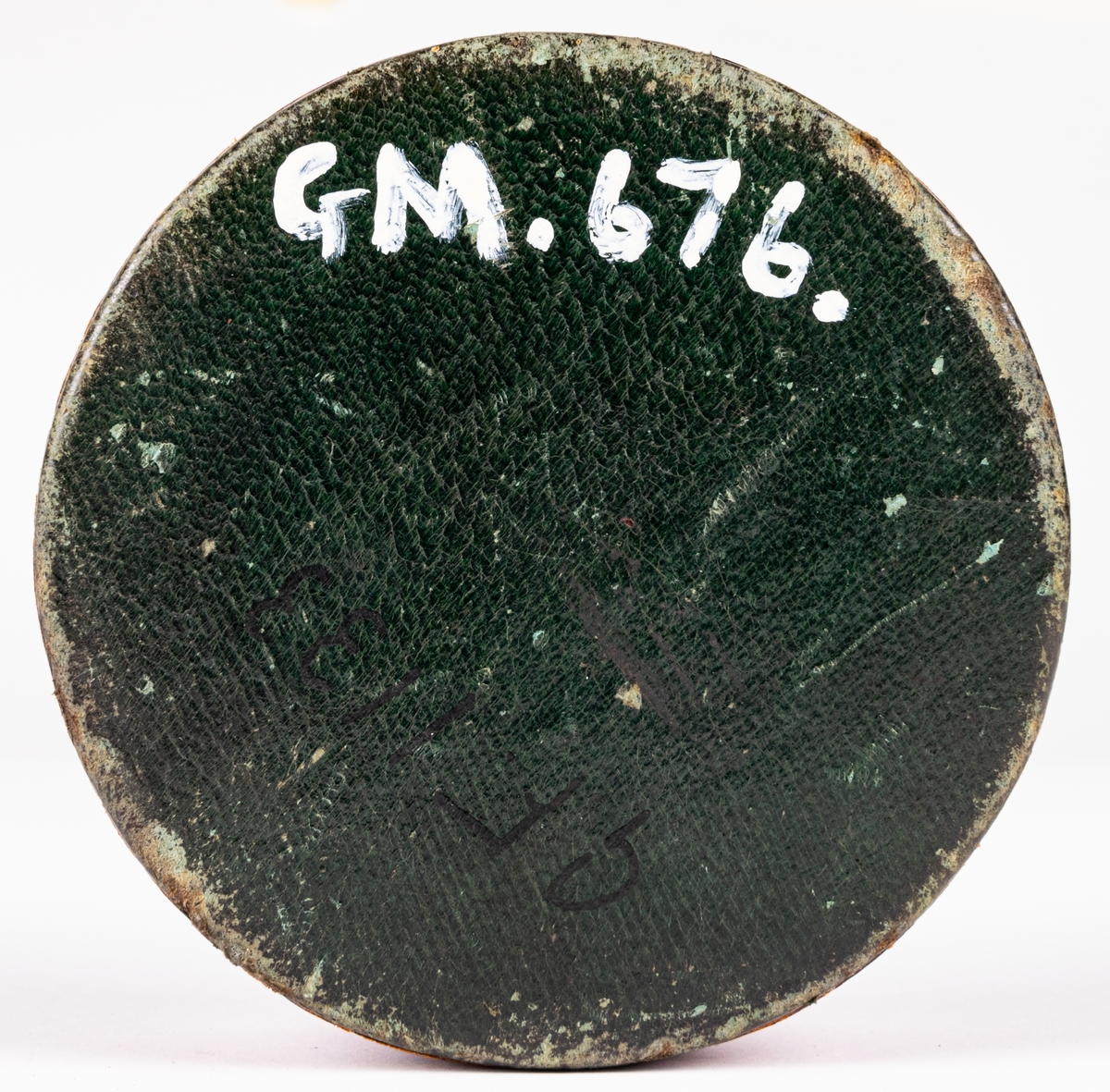 Tobaksask, låg, rund pappask, med botten av papp och lock av skinn skuret med snibbar och vridet koncentriskt så att snibbarna bilda en tiouddig figur. Sidorna röda, ovansidan skinnet grönt. Smala guldbårder på askens sidor och texten "Joh. Olof Norin", samt små guldstjärnor på ovansidan skinnet. Skinnet är saffian.