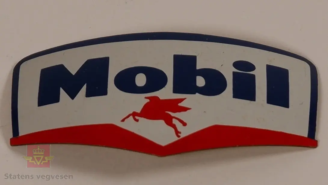 Mobil luemerke i metall med emaljert overflate. Hvit bakgrunn med Mobil skrevet i blått, rød pegasus med vinge i underkant. Luemerket har en buet form, og på baksiden er det er nål for festing til lue.
