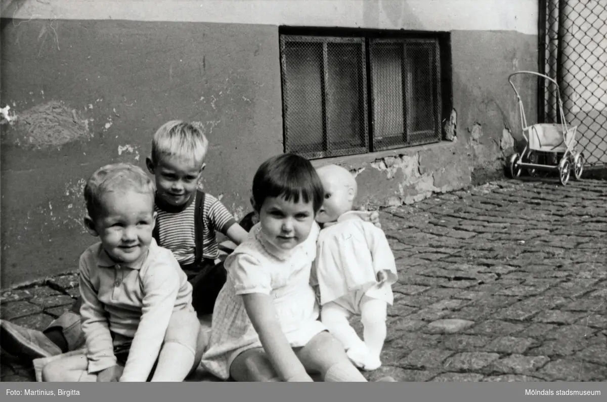 Tre barn sitter på innergården till Krokslättsgatan 3 år 1963. Från vänster: Kenneth Sjögren (1960 – 2017), kusinen Ilse Tobiasson (född 1960, gift Glimberg) samt deras kompis Jörgen Larsson (född 1958). Till höger ses Ilses dockvagn. Ilse och Jörgen var grannar på Krokslättsgatan 3 i Mölndal. Tvättstugan fanns där fönstrena ses i bakgrunden. På innergården brukade kvinnor träffas för att fika och bland annat knyta ryamattor. På den tiden var gårdarna uppdelade med flertalet staket (ses till höger). Mellan vissa gårdar fanns en låst grind som gjorde att man behövde gå runt byggnaden för att besöka andra i samma område. Vicevärden (Ella Johansson) hade nyckel till grinden. Barnen fick enbart leka på den inhägnade delen som tillhörde adressen. På varje gård fanns flertalet soptunnor, där råttor höll till.