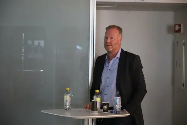 Mann snakker fra bord til publikum under åpning av utstilling.