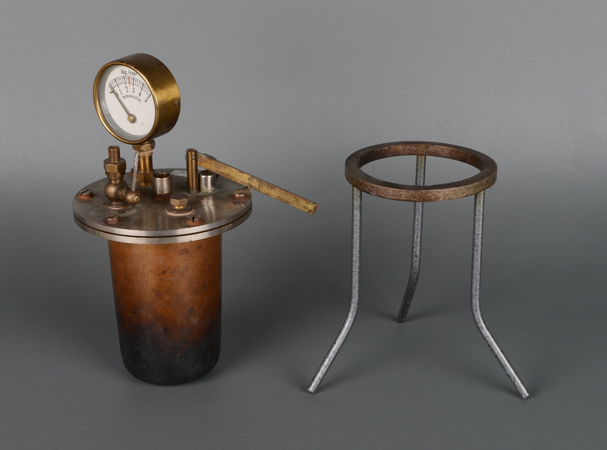 En trykktank av jern bestående av en kjeleformet tank som står i et rundt stativ med tre tynne bein. På toppen er det en måler av glass og messing for manometeret, som brukes inne i tanken til å måle trykk (kg/cm2). Måleskalaen går fra 0 til 5. Tanken er sylinderformet og lokket er skrudd fast med seks store skruer.