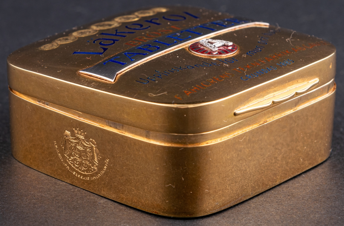 Tablettask i form av en Läkerolask, i guld med ädelstensinfattning i form av briljanter inlagda i bokstaven A på locket.
