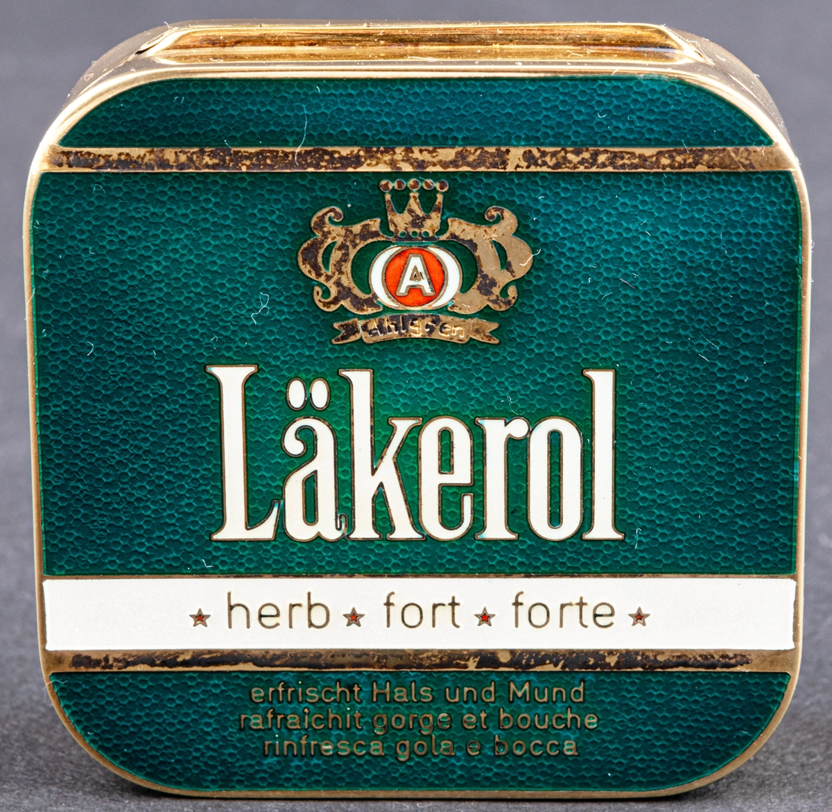 Tablettask av förgyllt silver med emalj med tillhörande rött etui i konstläder. Tablettasken har hämtat sitt utseende från den gröna Läkerolasken.