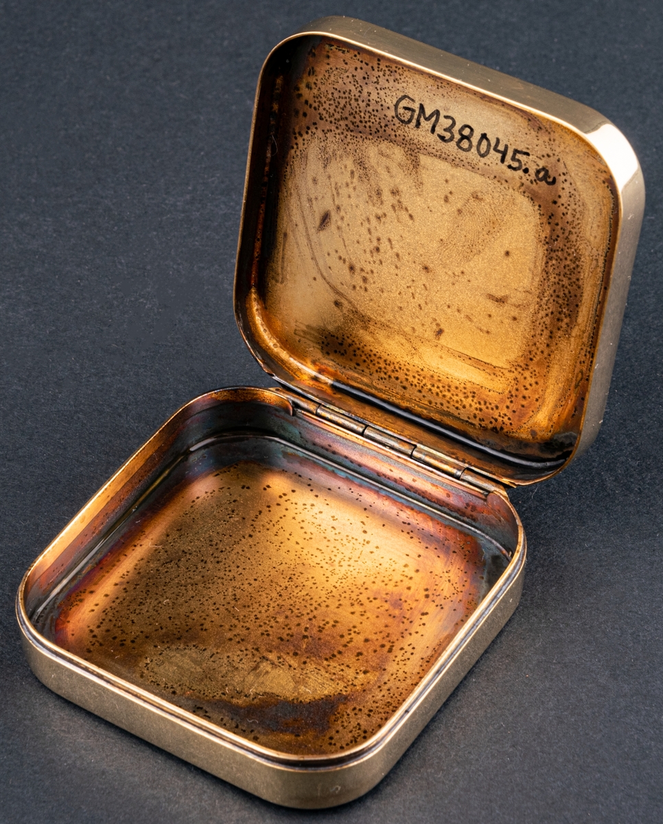 Tablettask av förgyllt silver med emalj med tillhörande rött etui i konstläder. Tablettasken har hämtat sitt utseende från den gröna Läkerolasken.