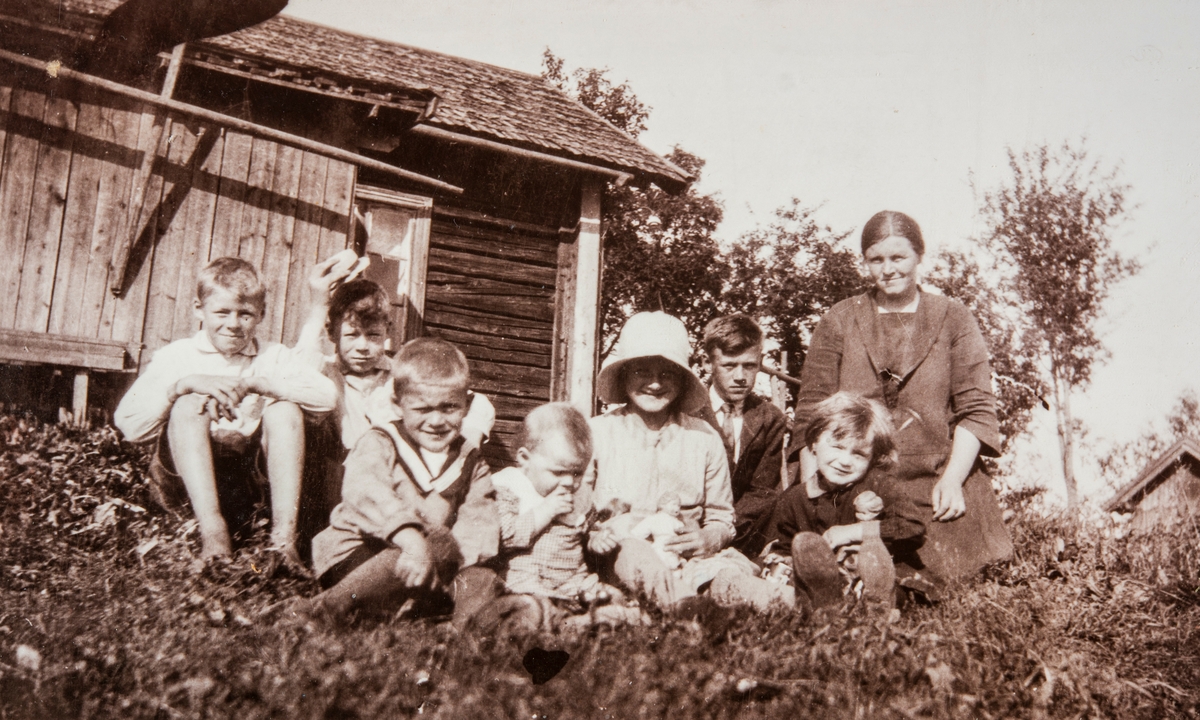 Gruppe 8 personer. Familiegruppe sittende foran stua i Roksvold, Ottestad.
Arvid, Mikkal, Toralf, Klara, Borghild, Alf, Margit og mor, Tora ???