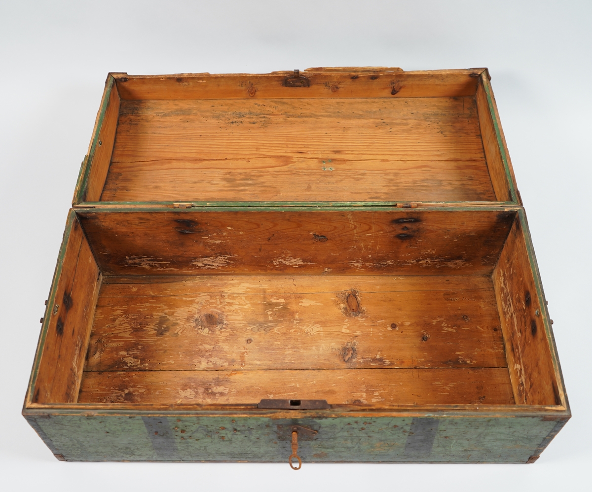 Ein grønmåla koffert i tre. Loket er forma av eit bord og er boga. Hjørna er halde saman med nokre "sinktapper" samt forsterka med metallvinkler. Kofferten har lås, og handtak i båe ender.