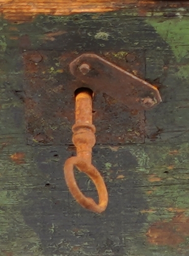 Ein grønmåla koffert i tre. Loket er forma av eit bord og er boga. Hjørna er halde saman med nokre "sinktapper" samt forsterka med metallvinkler. Kofferten har lås, og handtak i båe ender.