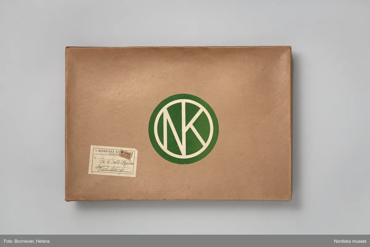 Paket från NK:s Franska damskrädderi.
När det handsydda plagget var avsynat och klart packades det ner med silkespapper i en NK-kartong innan budet tog vid. Stamkunden Elsa af Trolles klänning levererades med ilbud.